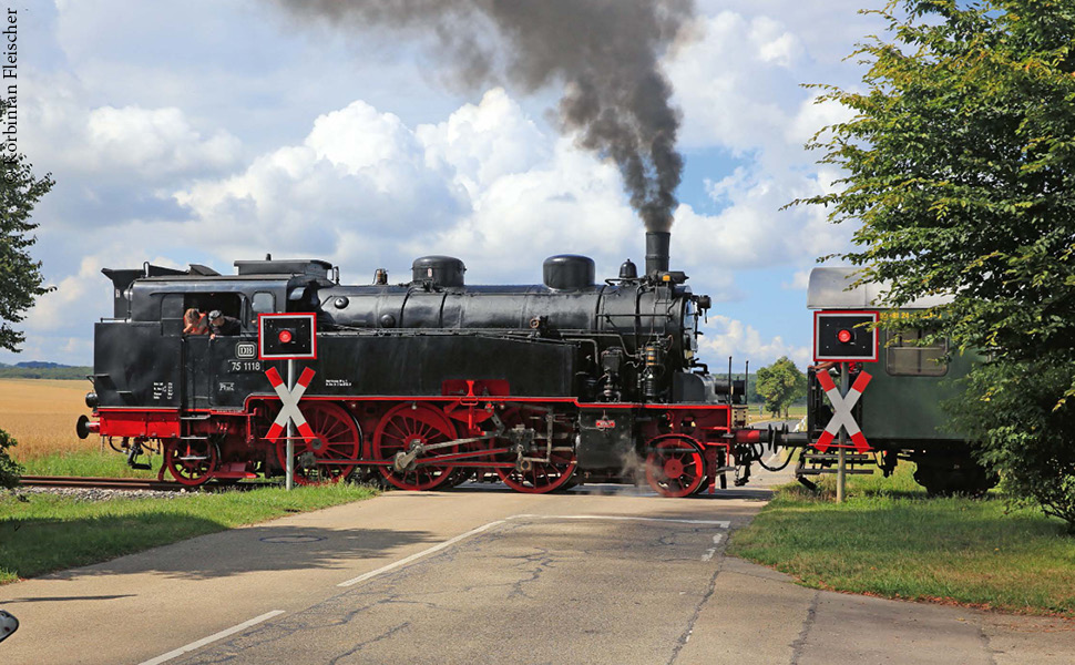 ein Dampfzug passiert einen  Bahnübergang