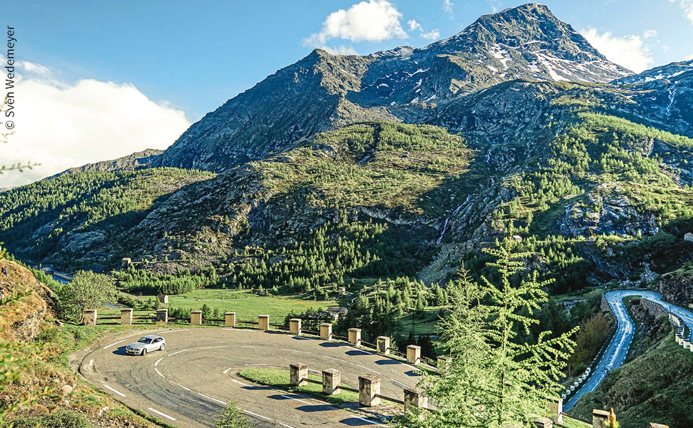 ein silberfarbenens Auto fährt die Serpentinenstraße unterhalb des Colle del Moncenisio entlag