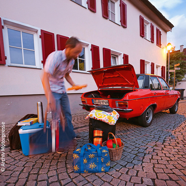 ein Mann packt Reisegepäck in den Kofferraum eines roten Autos