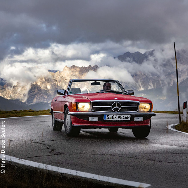 ein roter Mercedes-Benz 300 SL (R 107) mit stark bewölktem Himmel im Hintergrund