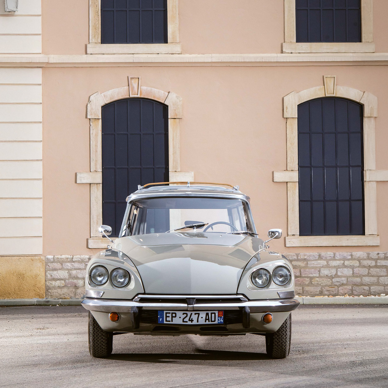 ein beigefarbener Citroën DS steht frontal vor einem Gebäude